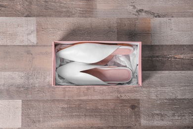 Photo of Pair of female shoes in box on wooden background, top view