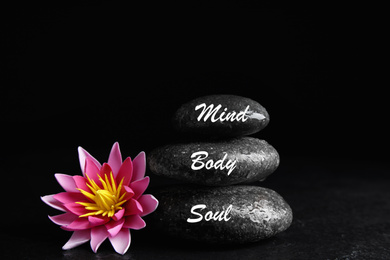 Photo of Stones with words Mind, Body, Soul and lotus flower on black background. Zen lifestyle