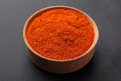 Aromatic paprika powder in wooden bowl on dark background