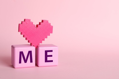 Phrase Love Me made with cubes and heart on pink background