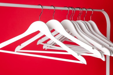 White clothes hangers on metal rack against red background, closeup