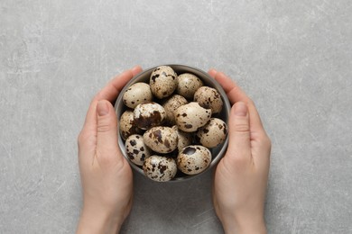 Woman holding bowl of quail eggs at light grey table, top view