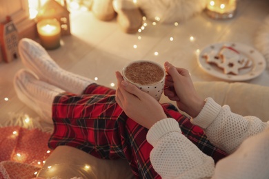 Woman with cup of hot drink at home, closeup. Christmas celebration