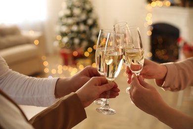 People clinking glasses of champagne in room decorated for Christmas, closeup. Holiday cheer and drink