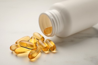 Overturned bottle with dietary supplement capsules on white table, closeup