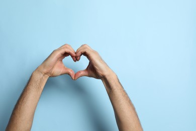 Man making heart with hands on light blue background, closeup. Space for text