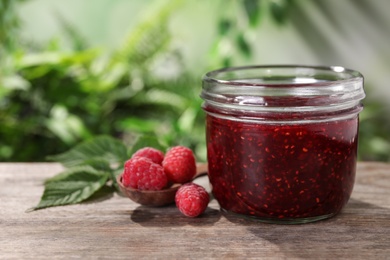Photo of Delicious jam in glass jar and fresh raspberries on wooden table