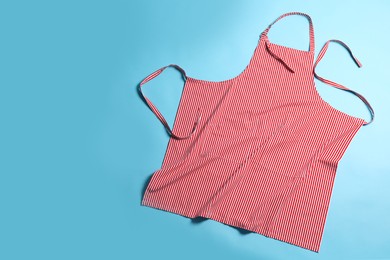 Photo of Striped apron on light blue background, top view. Space for text