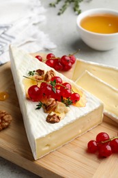 Brie cheese served with red currants, walnuts and honey on table, closeup