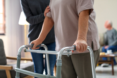 Care worker helping to elderly woman with walker in geriatric hospice, closeup