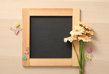 Blackboard, paper clips and flowers on wooden table, flat lay with space for text. Teacher's Day