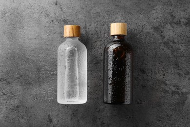 Bottles of cosmetic product on wet grey background, flat lay. Space for text