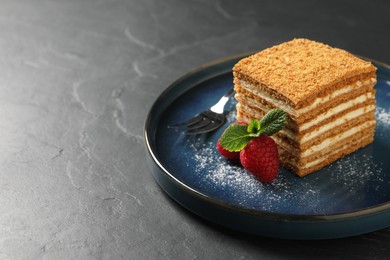 Slice of delicious layered honey cake with mint, raspberries and powdered sugar served on black table. Space for text