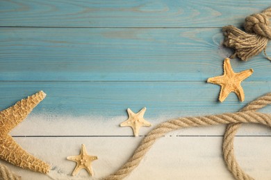 Beautiful sea stars, rope and sand on light blue wooden background, flat lay. Space for text