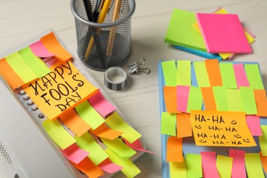 Corded phone and notebook covered with sticky notes on wooden table. April fool's day celebration