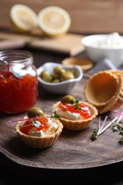 Photo of Delicious tartlets with red caviar and cream cheese served on wooden board, closeup