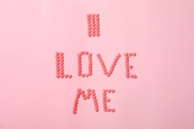 Phrase I Love Me made of heart shaped sprinkles on pink background, flat lay