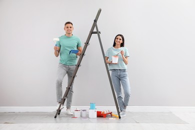 Young couple with decorator's tools near ladder indoors