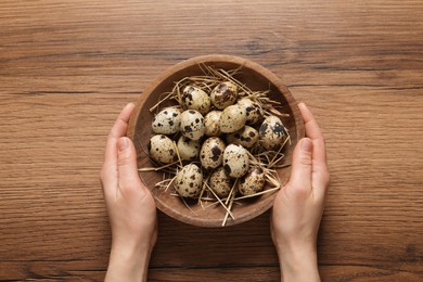 Woman holding bowl of quail eggs at wooden table, top view