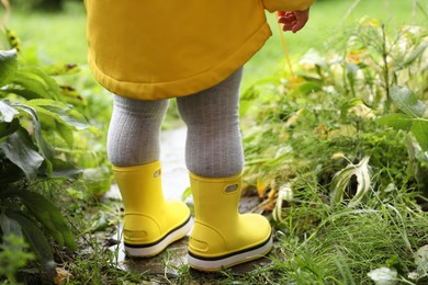 Little girl wearing rubber boots standing in puddle outdoors, closeup. Back view