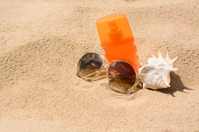 Photo of Bottle with sun protection spray, sunglasses and seashell on sandy beach, space for text