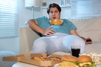 Overweight man with chips watching TV on sofa at home