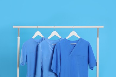 Photo of Medical uniforms on rack against light blue background