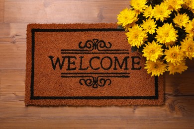 Photo of Doormat with word Welcome and beautiful flowers on wooden floor, flat lay