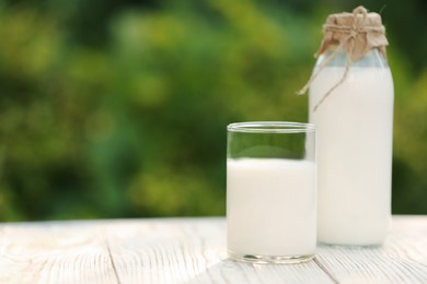 Bottle and glass of tasty fresh milk on white wooden table against blurred background, space for text