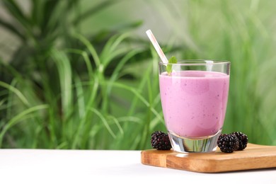Delicious blackberry smoothie in glass and berries on white table, space for text