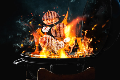 Meat and mushrooms falling onto barbecue grill with flame against black background, closeup