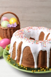 Glazed Easter cake with sprinkles and painted eggs on white wooden table, closeup