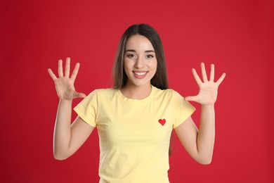 Woman in yellow t-shirt showing number ten with her hands on red background