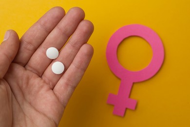 Girl holding pills near female gender sign on orange background, top view. Women's health