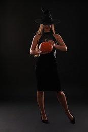 Young woman wearing witch costume with pumpkin on black background. Halloween party
