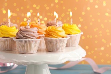 White stand with tasty birthday cupcakes on light blue wooden table against blurred lights, closeup