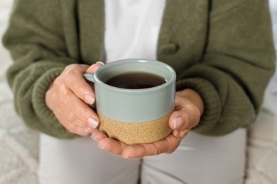 Elderly woman with cup of hot drink indoors, closeup. Home care service