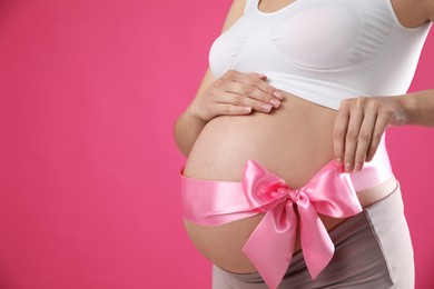 Young pregnant woman with bow on her belly against pink background, closeup and space for text. Time to give birth