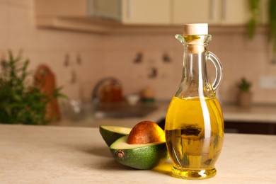 Photo of Fresh avocado and jug of cooking oil on beige table in kitchen, space for text