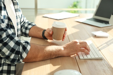 Freelancer with cup of coffee working on computer at table indoors, closeup