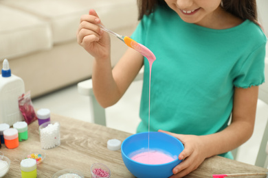 Little girl mixing ingredients with silicone spatula at table indoors, closeup. DIY slime toy