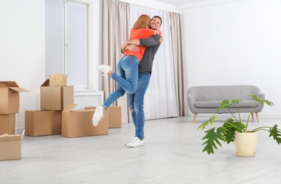Happy couple hugging near moving boxes in their new house