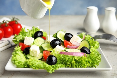 Dressing tasty fresh Greek salad with olive oil on grey table
