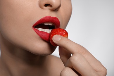 Photo of Young woman with beautiful lips makeup eating strawberry on light background, closeup