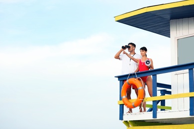 Lifeguards with megaphone and binocular on watch tower against blue sky