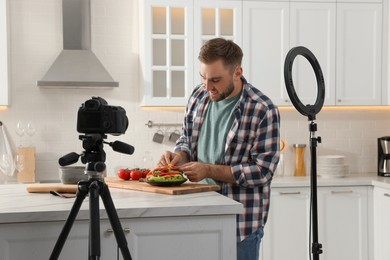 Blogger with tasty croissant recording video in kitchen at home. Using ring lamp and camera