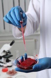 Photo of Scientist dripping red liquid into Petri dish with raw cultured meat in laboratory, closeup