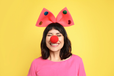 Photo of Joyful woman with large bow and clown nose on yellow background. April fool's day