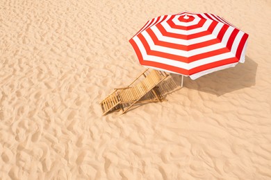 Striped beach umbrella near wooden sunbed on sandy coast