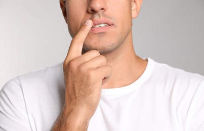 Man with herpes touching lips against light grey background, closeup